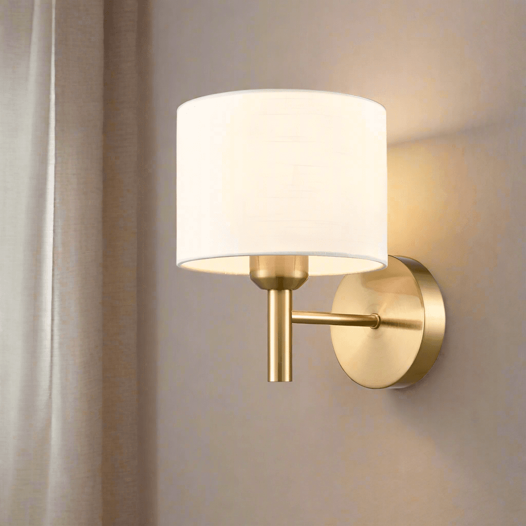 Really stylish aged brass metal fixture wall light with a round cream shade creating an instant classy and elegant feel. The fabric shade is in a soft white or cream colour. The subtle texture on the fabric adds depth without overwhelming the design. It would work beautifully in a bedroom, hallway, or living area; especially in interiors with brass accents or warm neutral palettes.