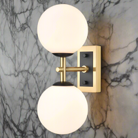 A wall-mounted dual light fixture with one aged brass and one matt black metal fixture, each with a round opal glass globe.
