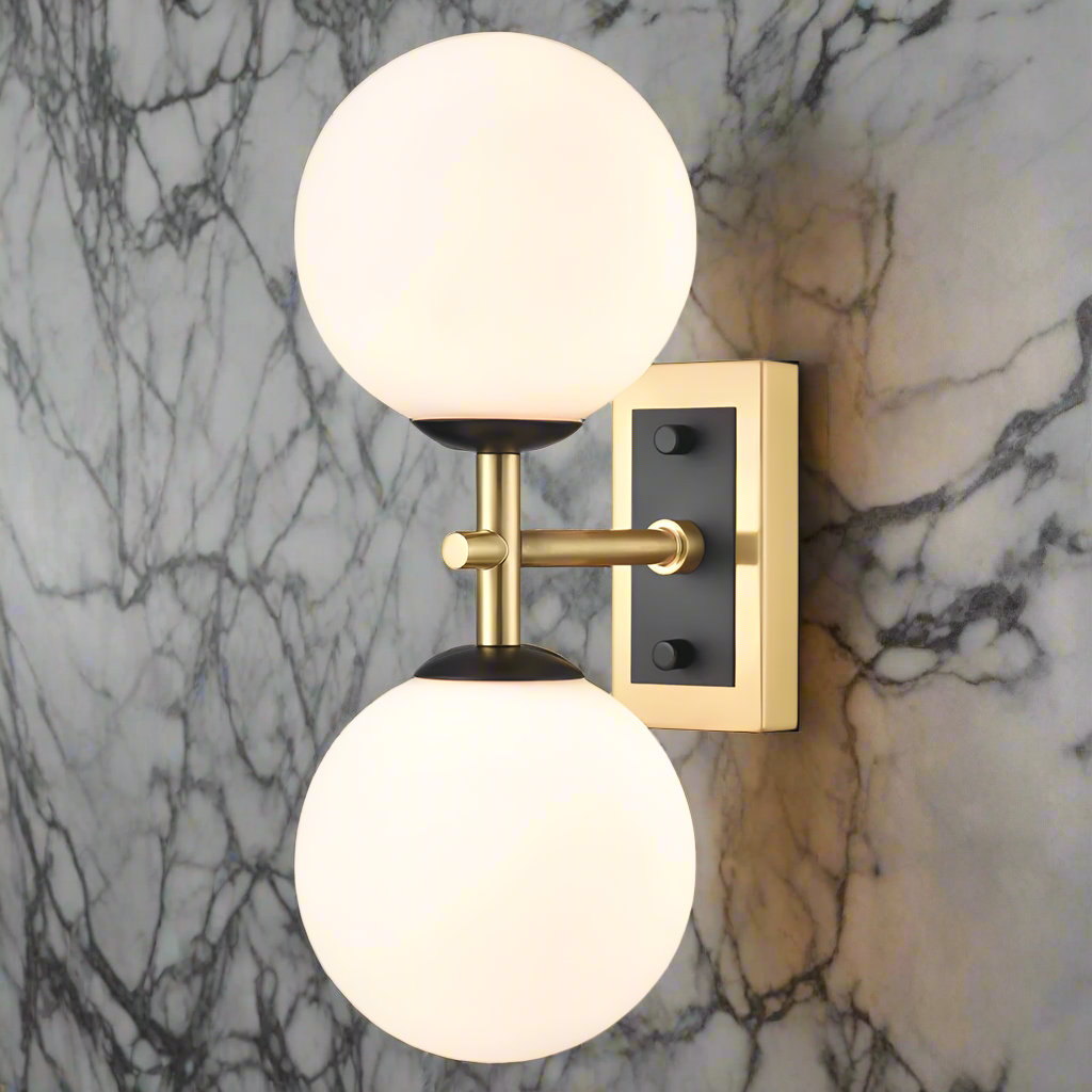 A wall-mounted dual light fixture with one aged brass and one matt black metal fixture, each with a round opal glass globe.