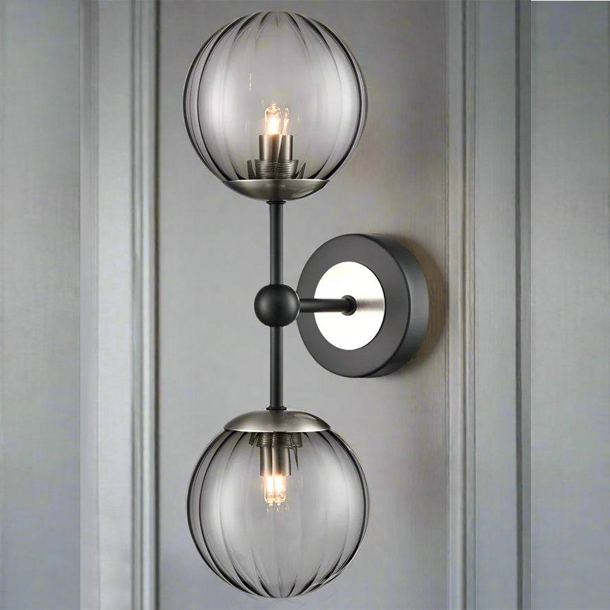 A very smart black double globe ribbed glass ball wall light with black iron and brushed nickel metal arms and circular wall plate. 
With deco tones, this contemporary wall light easily complements any interior style.  Discreet black ribbed glass globe balls mean that light can be softly diffused from the warm white G9 bulbs that can be purchased separately from our site.  
This black ribbed glass wall light seamlessly integrates into any space without over dominating. 
