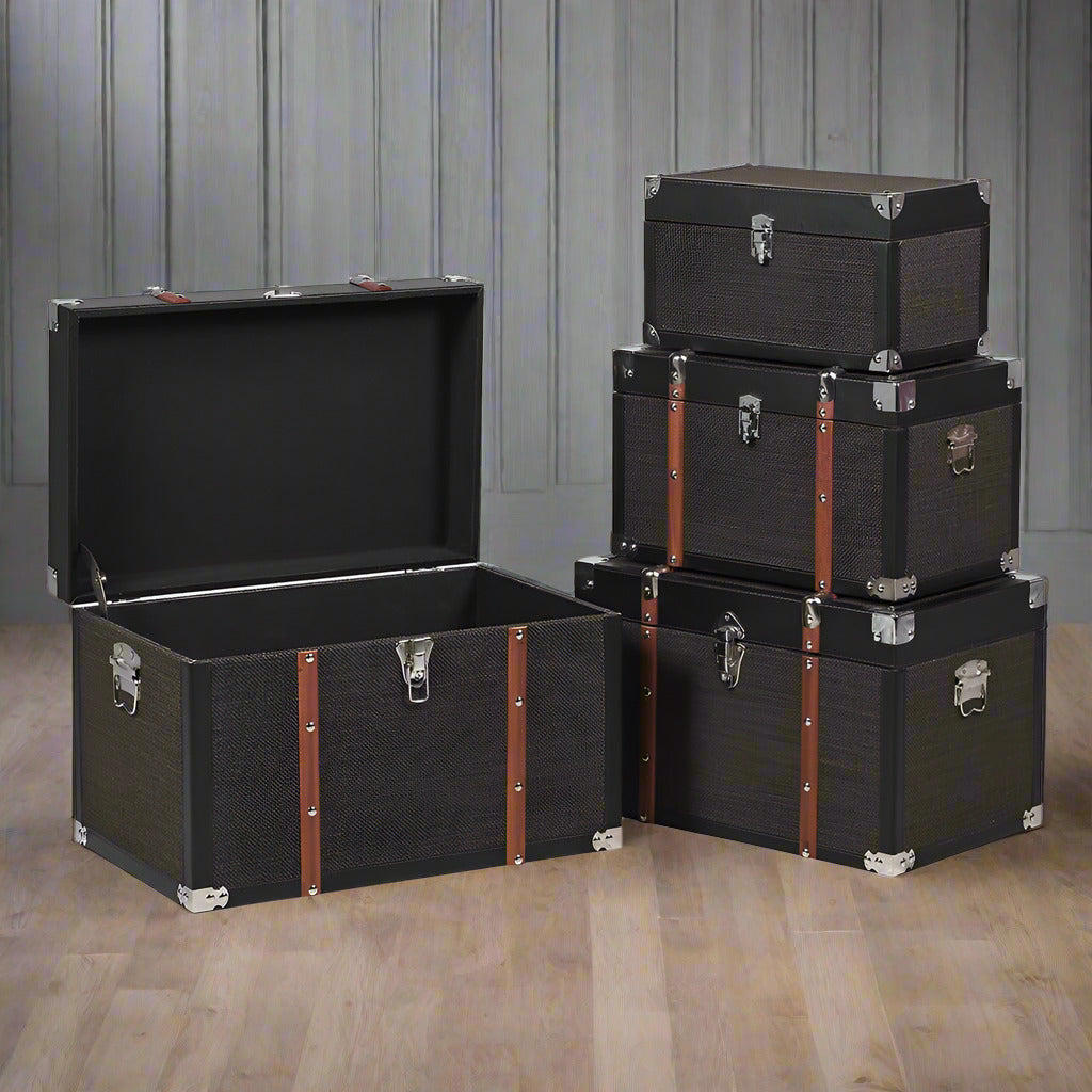 Set of four black trunks in varying sizes.  The three larger trunks are banded with wooden straps and nickel studs. Trunks are such a useful item of furniture, perfect for storage but can also be used as a side table in a living room, bedroom study or for storing shoes in a hall. The black hessian covering will work in so many interiors