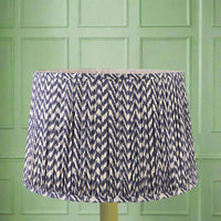 A large, chevron patterned, pleated lampshade in blue and cream colors, displayed against a green background.