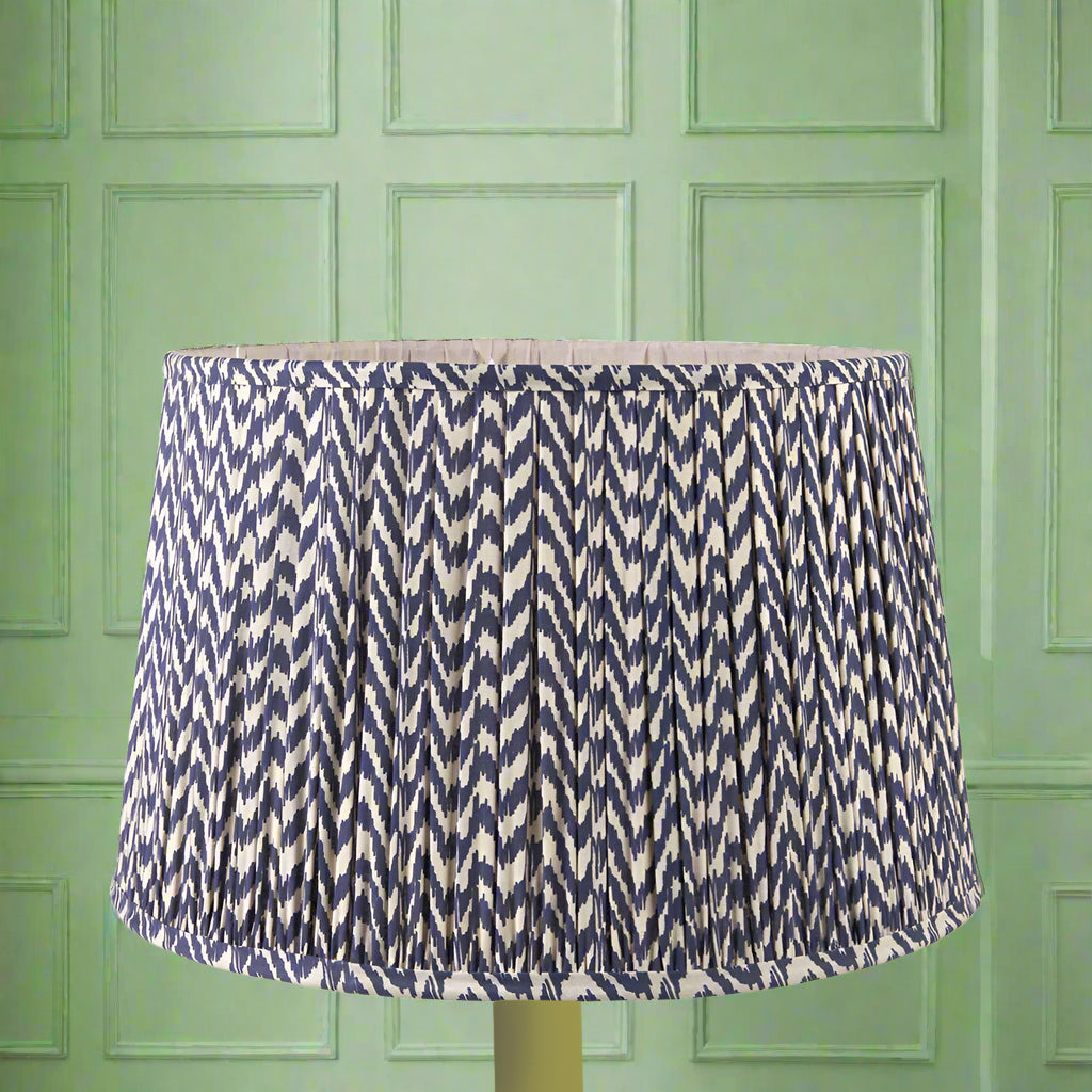 A large, chevron patterned, pleated lampshade in blue and cream colors, displayed against a green background.