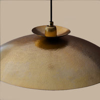 Modern pendant featuring a hammering brass metalwork finish with a black flex. This brass disc pendant light is a striking, contemporary lighting fixture that combines sleek design with industrial charm. Its wide shape allows the light to spread evenly across any room. It is a very stylist and ideal for living rooms.