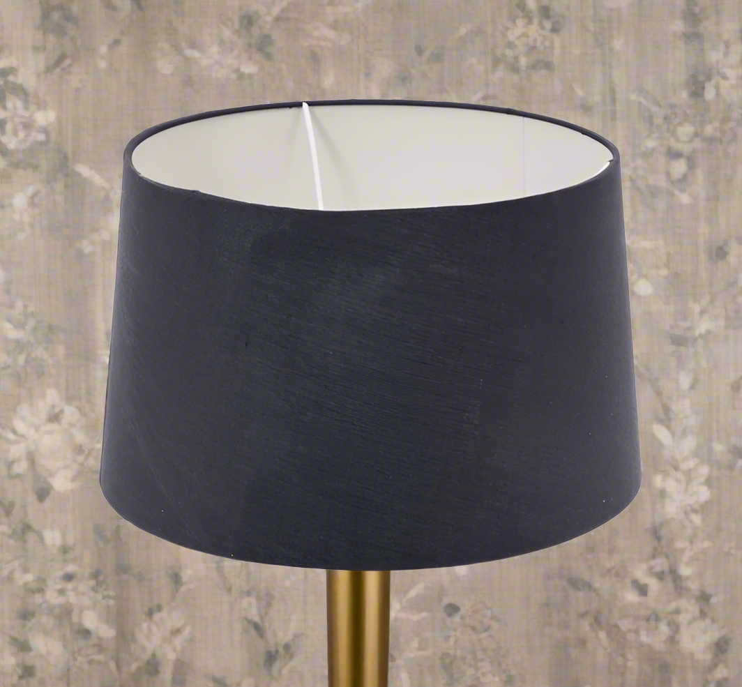 A charcoal gray lamp shade with a white inner, placed on a lamp base, against a floral patterned background.