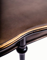 Medium size curved metal console table with pale gilt accents to the rim or the top. The curved metal frame of this black table adds a soft sculptural element.