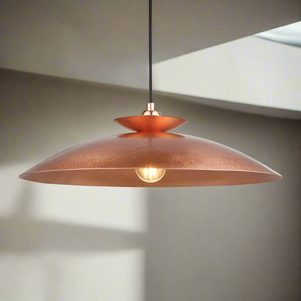 Modern pendant featuring a hammering copper metalwork finish with a black flex.  This copper disc pendant light is a striking, contemporary lighting fixture that combines sleek design with industrial charm. Its wide shape allows the light to spread evenly across any room. It is a very stylist and ideal for living rooms, bedrooms and kitchens