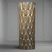 A tall brass-colored metal umbrella stand with a geometric pattern