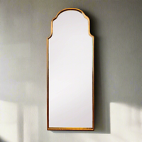 An arched metal shaped gilt mirror mounted on a wall, with a simple rectangular frame.