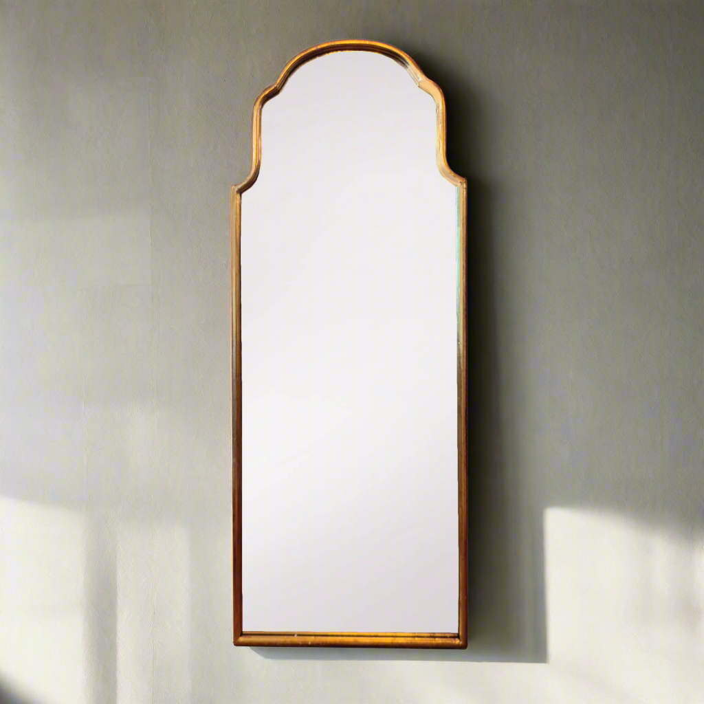 An arched metal shaped gilt mirror mounted on a wall, with a simple rectangular frame.