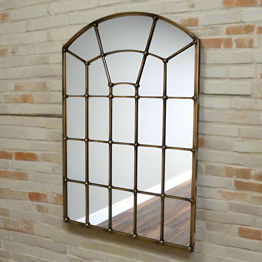 A great arched metal window mirror in an antique brass finish with studding to the frame. Like all window mirrors this one will give the impression that the room in which it hangs is larger and brighter.  An unusual colour and the studs on the frame adding an industrial feel. 