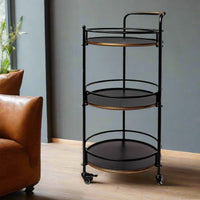 Black metal serving cart with gold accents in a room with a brown leather chair and gray wall.