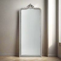 A tall, narrow silver framed mirror with decorative applique to the crown. A really pretty but substantial mirror, perfect for a bedroom or dressing room, leaning against the wall, it will add luxury and glamour to your space.