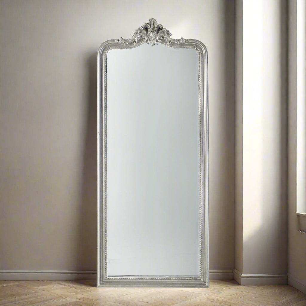 A tall, narrow silver framed mirror with decorative applique to the crown. A really pretty but substantial mirror, perfect for a bedroom or dressing room, leaning against the wall, it will add luxury and glamour to your space.