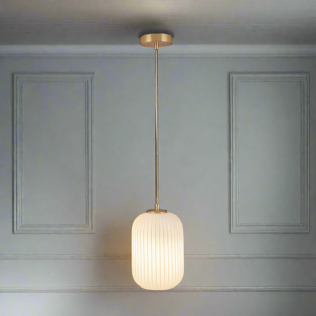 Long white glass pendant with a soft gold fitting and ceiling rose.    Opaque glass has the benefit of offering a warm diffused glow in a room, perfect in a bedroom, hall or living room where warm, welcoming lighting is a must. The other benefit of opaque pendants is that they hide the bulbs.
H: 150 cm W: 15 cm