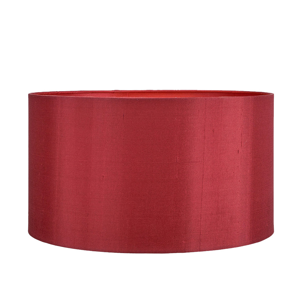 A red silk lampshade with a drum shape, positioned on a stand against a green background.