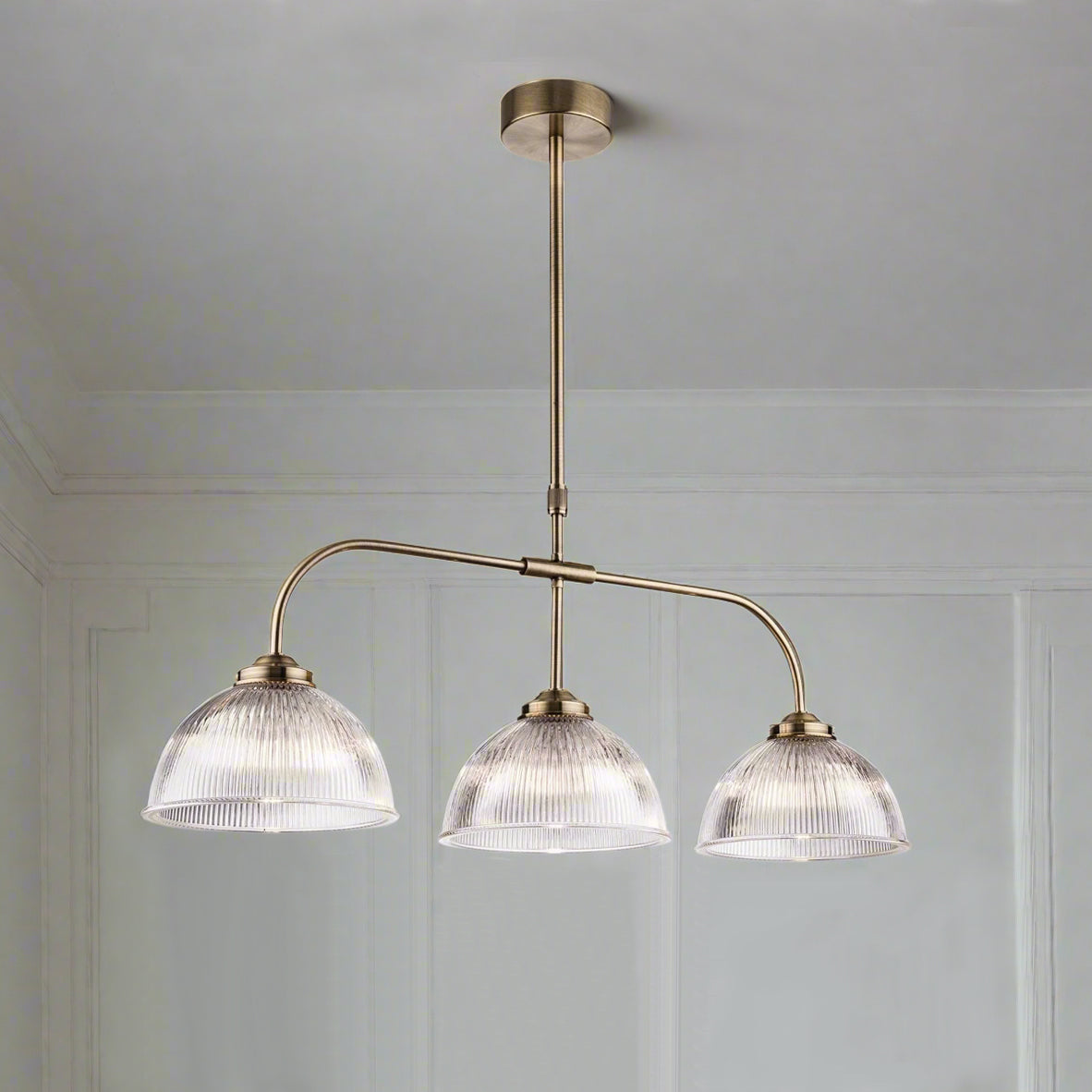 Three ribbed glass pendants on a fixed antique brass frame, perfect traditional light for a period house, over a kitchen island, dining table or even a billiard table. Linear lighting is a great way to light the darkest of rooms, the light spreading from the three shades, and this particular linear light is glamorous enough for any room in your home.