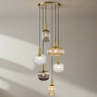 A cluster pendant light with six ribbed glass shades in varying subtle colored shades, suspended from a circular brass fitting.