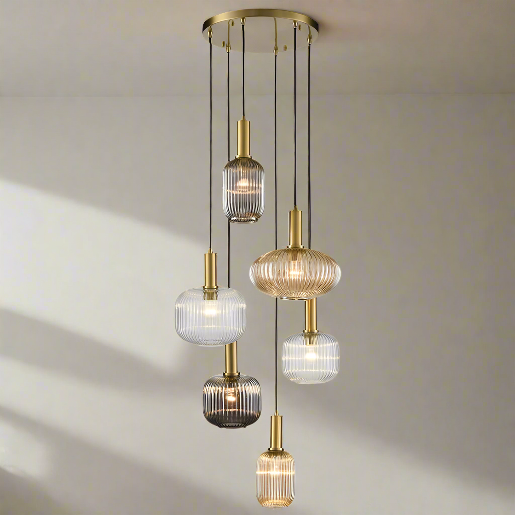A cluster pendant light with six ribbed glass shades in varying subtle colored shades, suspended from a circular brass fitting.