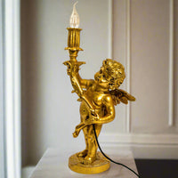 Gold cherub table light, perfectly formed cherubim hand outstretched holding a lamp.  The lamp looks best with the addition of a filament bulb to add a glow.  The lamp has a rococo decorative style working well in a luxurious bedroom, baroque styled living room - anywhere you need a touch of glamour.   So decorative but also perfectly functional.  