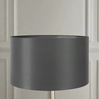 A gray silk lamp shade on a lamp, with a textured pattern. The shade is displayed in a home environment, likely a living room setting.