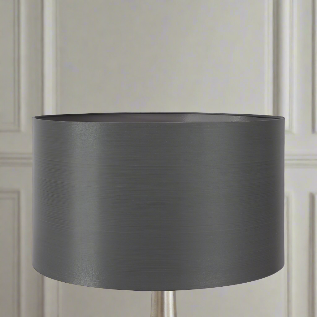 A gray silk lamp shade on a lamp, with a textured pattern. The shade is displayed in a home environment, likely a living room setting.