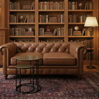 A set of two, bronze topped round side tables in a library setting with leather sofa, stacked bookcases and lamp.