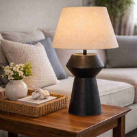 The sculptural black base features a subtle textured finish, beautifully contrasted by a soft neutral fabric shade that diffuses light gently throughout the room. Its balanced proportions make it a versatile piece that complements both modern and classic interiors.