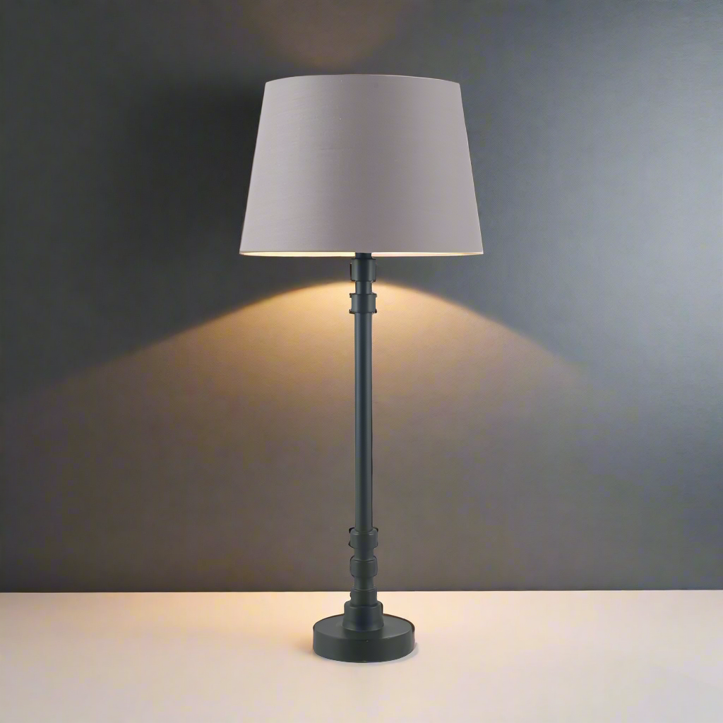 A black metal table lamp with a traditional design, featuring a lamp base without a shade, standing on a white surface against a dark background.