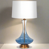 Glass ombre coloured lamp base with a darker blue base fading to clear nearer the white shade. The lamp is centred onto a gilt base. Classic contemporary look.