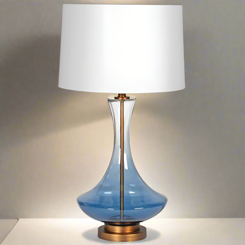 Glass ombre coloured lamp base with a darker blue base fading to clear nearer the white shade. The lamp is centred onto a gilt base. Classic contemporary look.