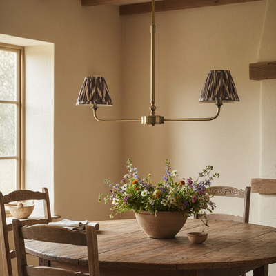 A refined ceiling light featuring an brass frame with two curved arms, each supporting a classic tapered fabric clip shade. 