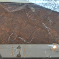 Detailed view of the mirrored shelf of a brass Empire-style side table with visible scratches and imperfections.