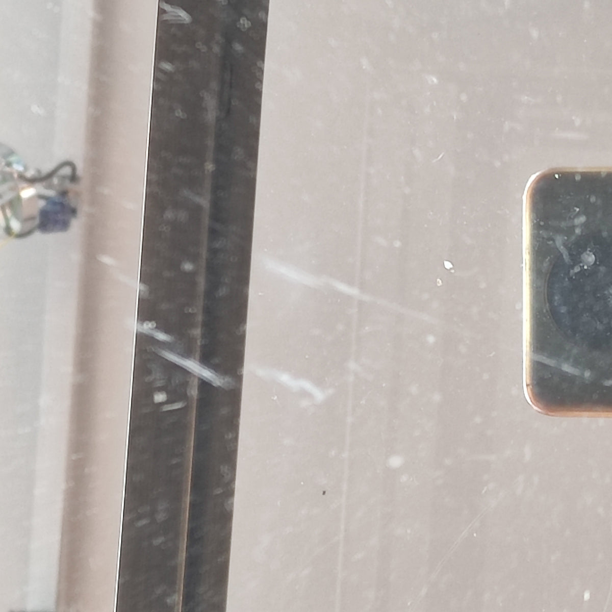 Close-up of the glass top of a brass Empire-style side table showing scratches and wear on the surface.