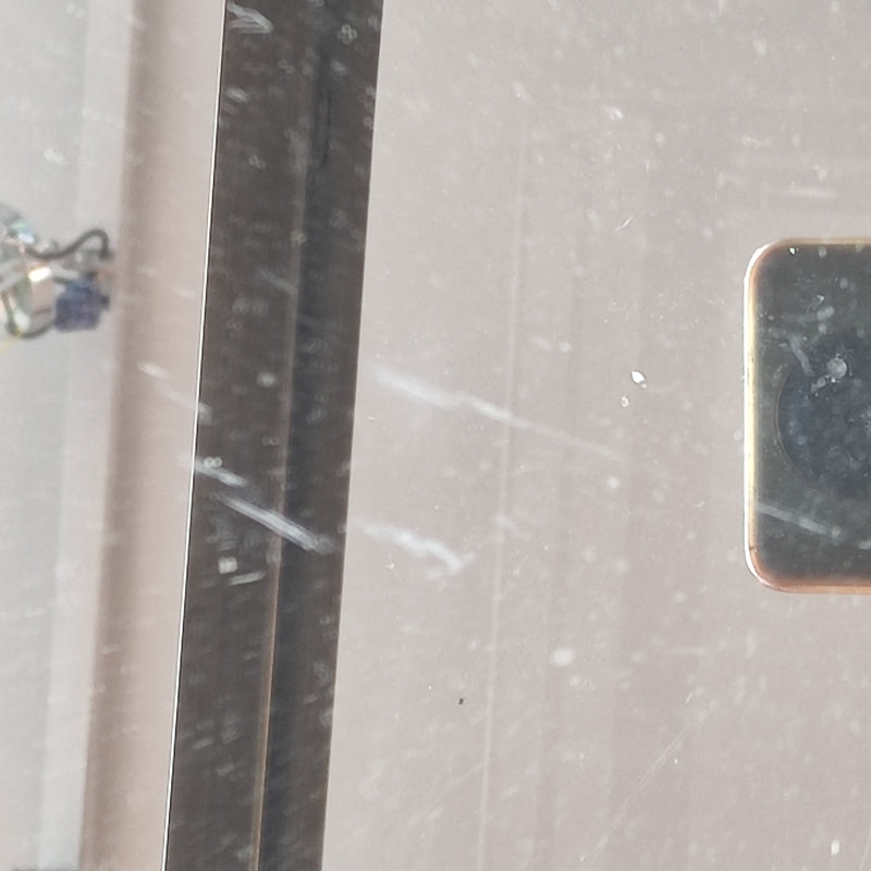 Close-up of the glass top of a brass Empire-style side table showing scratches and wear on the surface.