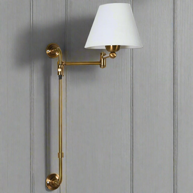 Long brass wall light with white fabric shade. The light is adjustable and can slide up the brass pole to be placed where needed. An elegant, tall wall lamp that would look good in any space, perfect for a living room wall or as extra bedroom lighting.