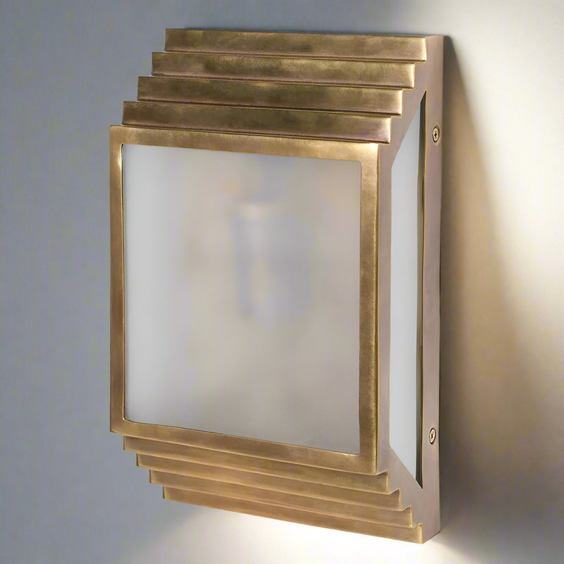 A brass wall light in the shape of a stepped brushed brass box, with a frosted front.&nbsp; The overall effect of this stunning wall light is of the 'art deco' period, the box construction with the frosted glass detail to the front.&nbsp; The lamp can be hung vertically or horizontally and will exude a beautiful muted light. Two of these on your wall will create a dramatic, stylish effect.