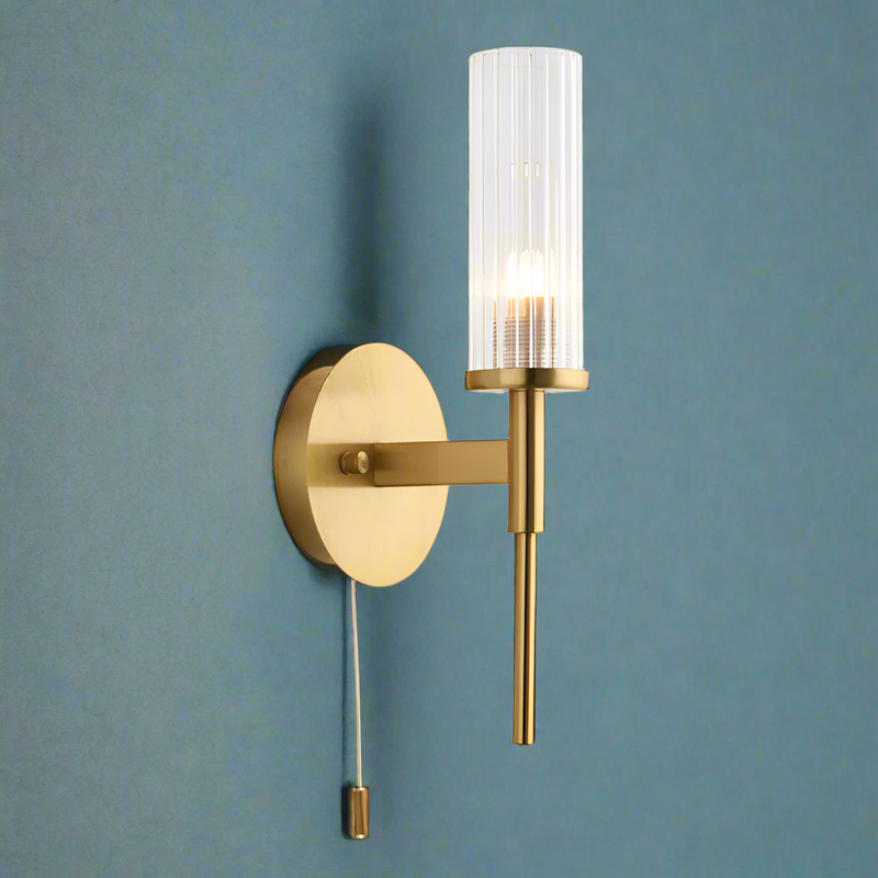 This stylish brushed gold and ribbed clear glass wall light has a IP44 rate. It is suitable for bathrooms and has a pull cord. It creates an instant classy and elegant feel.