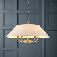 An antique brass chandelier with a white linen shade, featuring five light bulbs, hanging from a gold chain.
