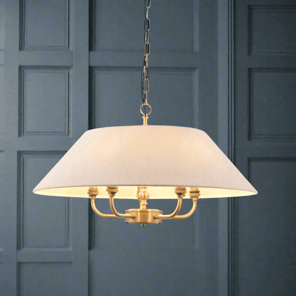 An antique brass chandelier with a white linen shade, featuring five light bulbs, hanging from a gold chain.