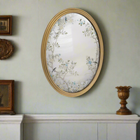 A decorative gilt framed oval wall mirror painted in the 'Victorian' style with floral motifs. A light-enhancing reflective glass surface. 