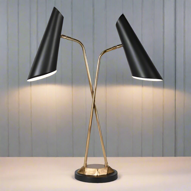A double table lamp with black metal base and dual black shades, standing on a circular base. The lampshades are positioned at an angle, providing illumination.