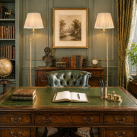 Elegant home office with green leather tufted armchair, antique wooden desk, classic brass floor lamps with shades, and vintage decor