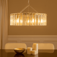 Contemporary glass chandelier with five lights, vertical glass rods and a gilded frame, in a lit dining room