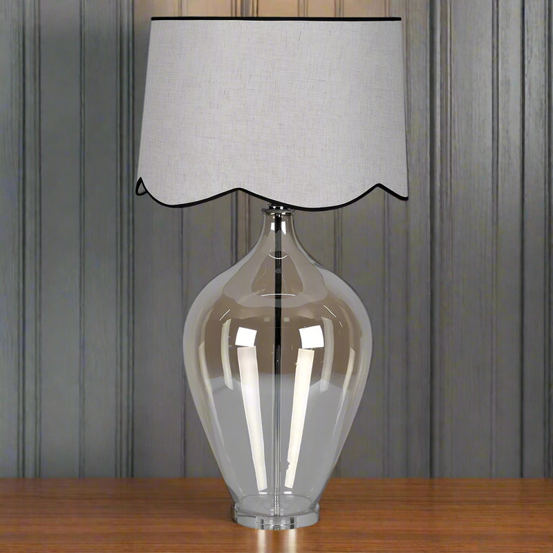 This table lamp has an unusual luminescent, ombre style glass base in an urn shape.&nbsp; It is polished and clear to give a clean, modern look whilst still allowing light to reflect&nbsp; through it. The empire style shade with a scalloped lower edge adds a soft decorative detail tat contrasts with the clean lines of the glass base.&nbsp; The overall effect is of a traditional elegance with a modern twist. A really tall statement lamp and shade.