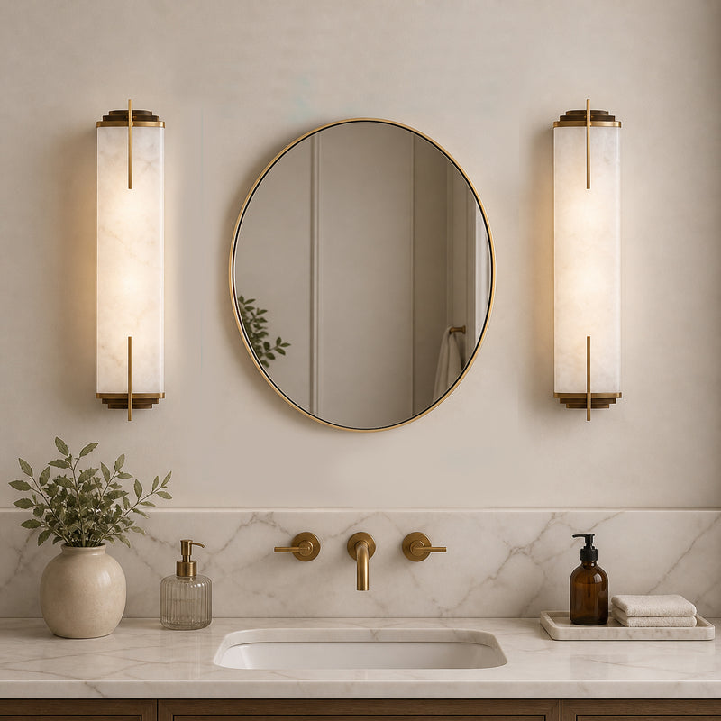 Gilt oval mirror between two art deco bathroom lights, over a marble sink in a classic bathroom.