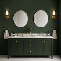 Two oval gilt framed mirrors above a double sink unit in a deep olive coloured bathroom. 
