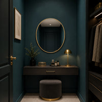 Gilt oval mirror in a cloakroom setting, dark teal painted walls with dressing table and lights.