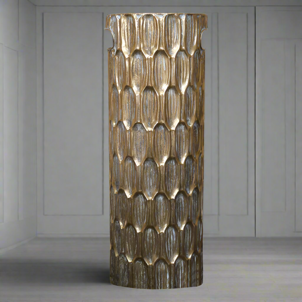 A tall brass-colored metal umbrella stand with a geometric pattern