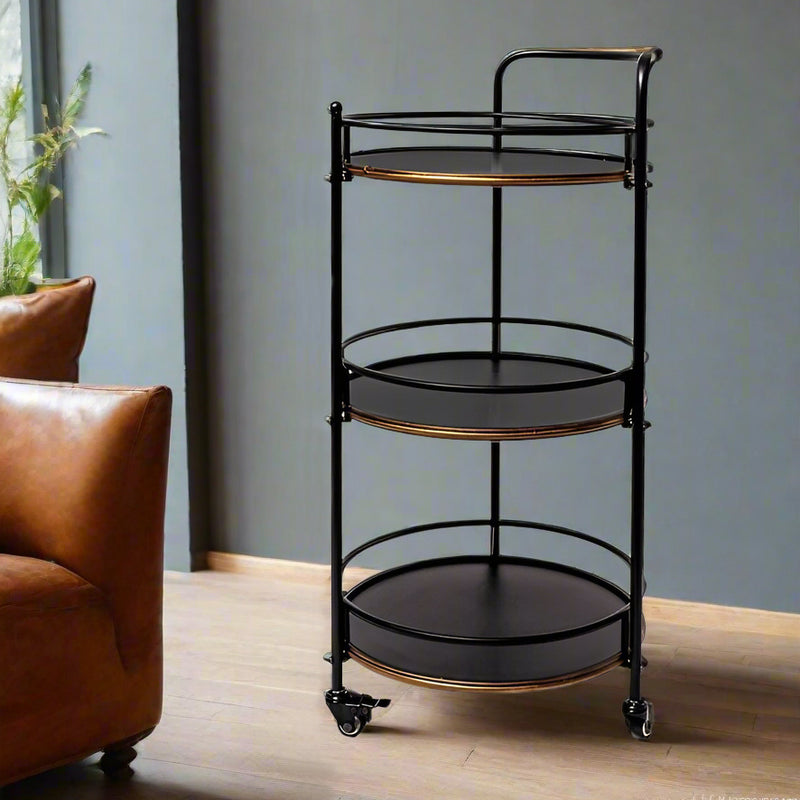 Black metal serving cart with gold accents in a room with a brown leather chair and gray wall.